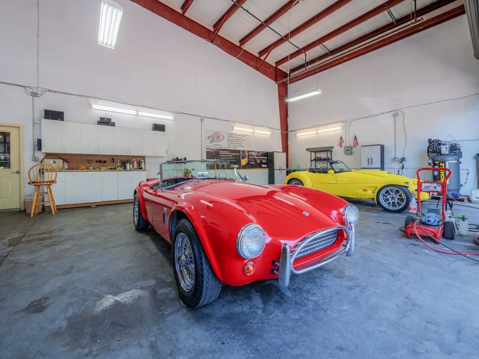 A red Cobra-style roadster in the A1 detailing bay, with a yellow roadster behind it.