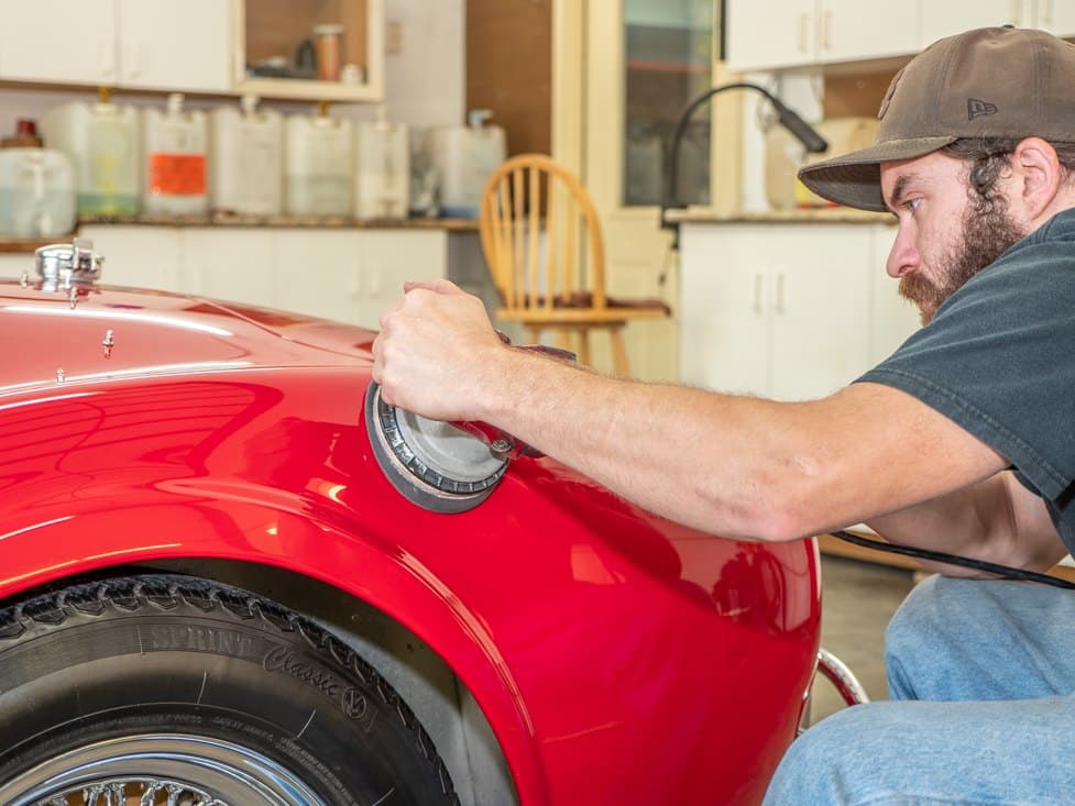 An A1 detailer machine-polishing the fender of a red roadster.