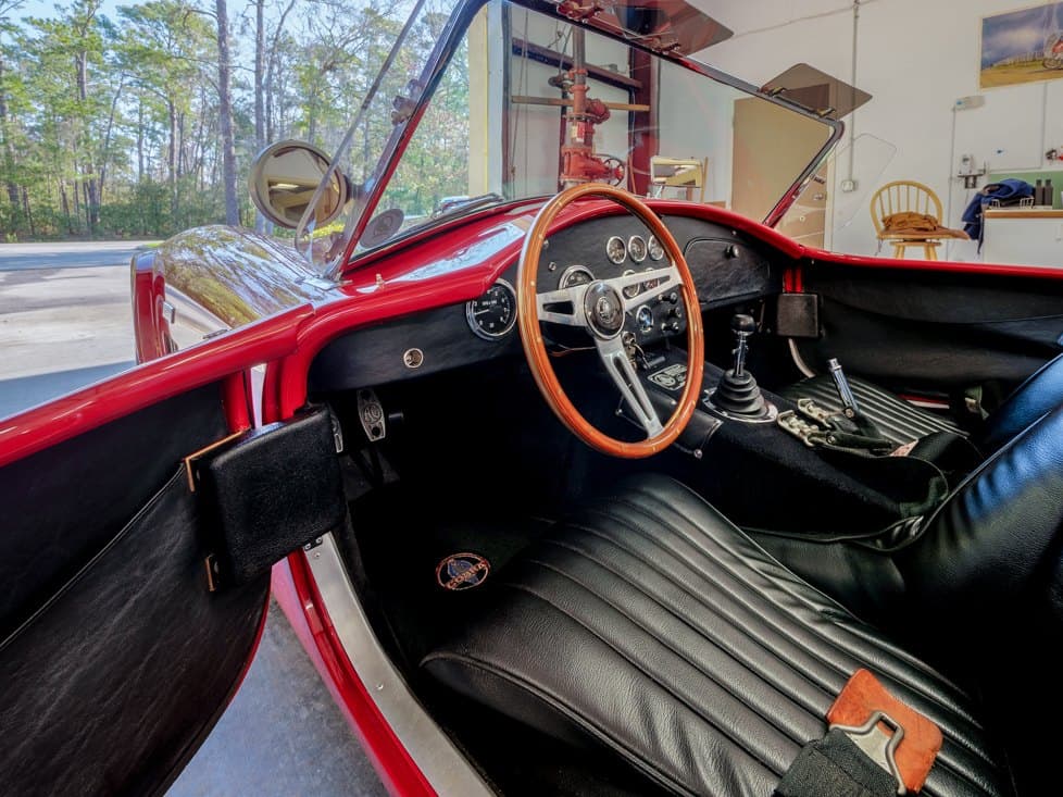 The cockpit of a red roadster after detailing: wood steering wheel, gauges and black leather seat.