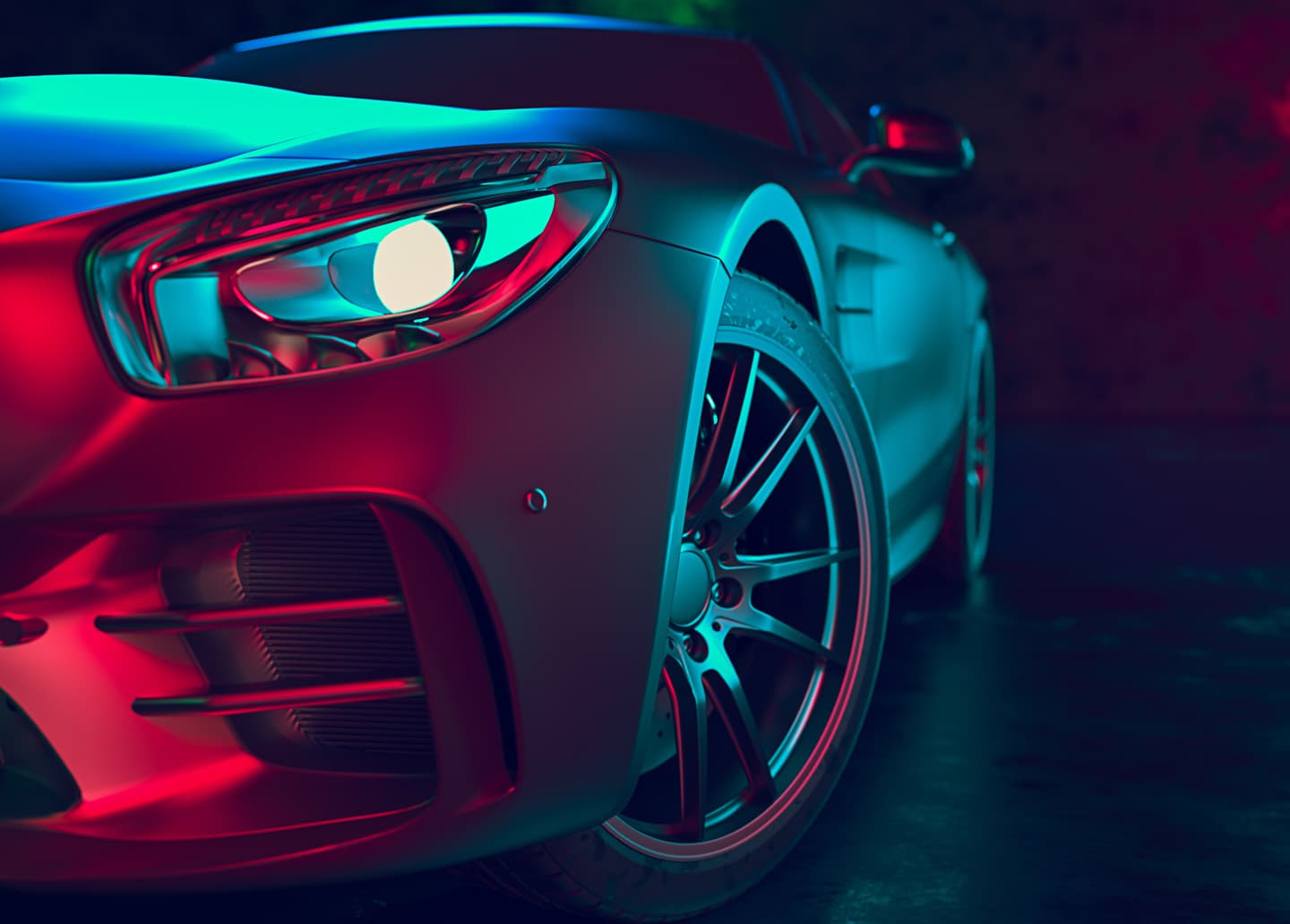 Front corner of a sports car lit in red and blue, headlight and alloy wheel in sharp focus.